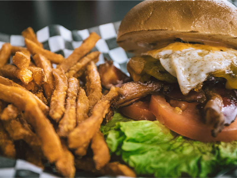 A photo of a very scrumptious bacon and egg cheeseburger with a side of freshly fried yam fries.